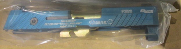 A long rectangular blue piece of metal, covered in transparent plastic is shown. It is a slide that is
used in the C24 pistol designed to fire simulated munitions for training purposes.